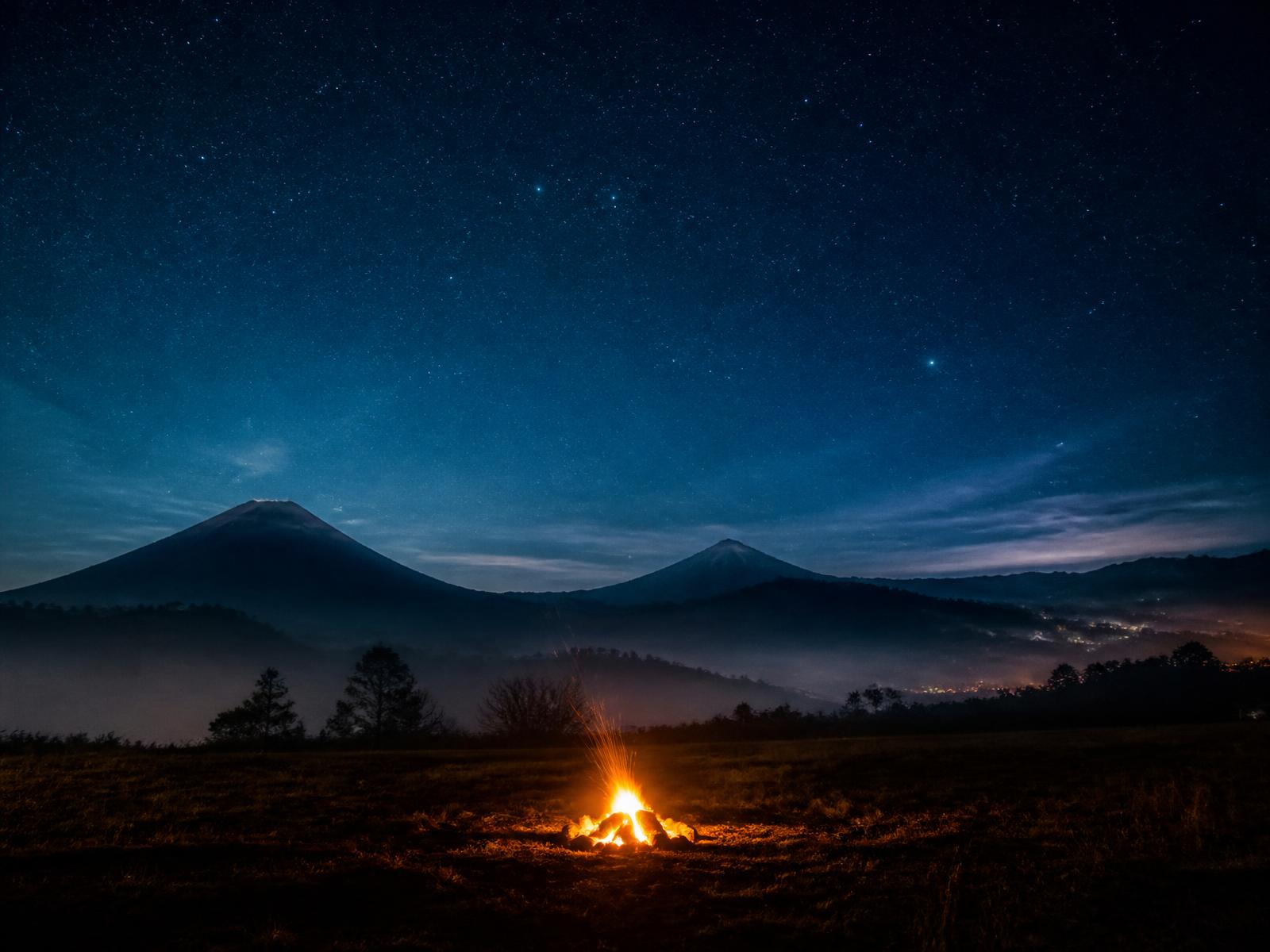Noche estrellada sobre las montañas de Xela, Guatemala, con una fogata encendida